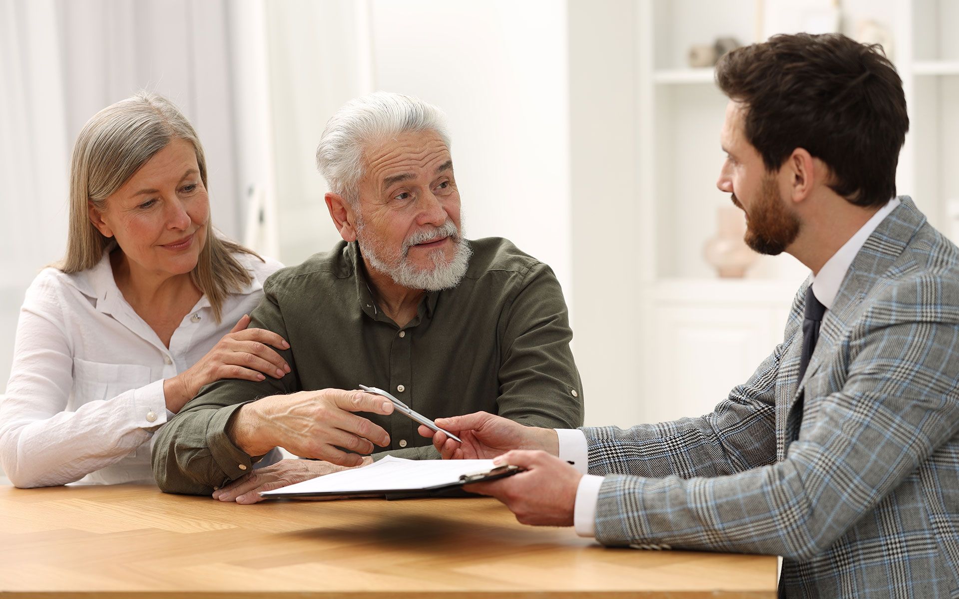 A senior couple signing a document with a younger man, likely a professional, at a table in a home.