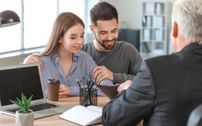 Couple at a desk with a person in a suit, likely meeting with a financial advisor. The couple appears happy.