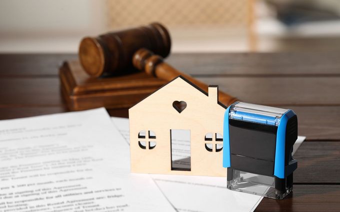 A wooden house cutout, documents, a gavel, and a stamp on a wooden table, symbolizing real estate or legal proceedings.