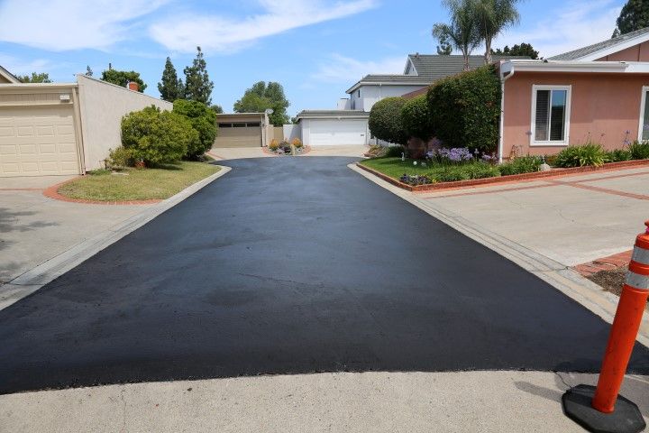 Freshly paved asphalt driveway in residential area; houses and garages visible under a blue sky.