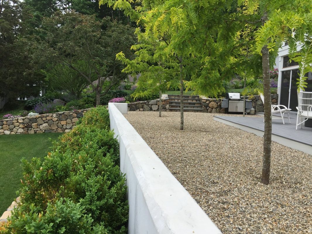 Stone wall and trees in a landscaped yard; a concrete retaining wall in the foreground.