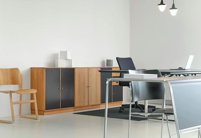 Office with desk, chairs, wooden storage cabinets, laptop, and pendant lights.
