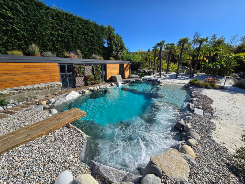 Piscina con acqua turchese e limpida, trampolino in legno e piccola cascata.