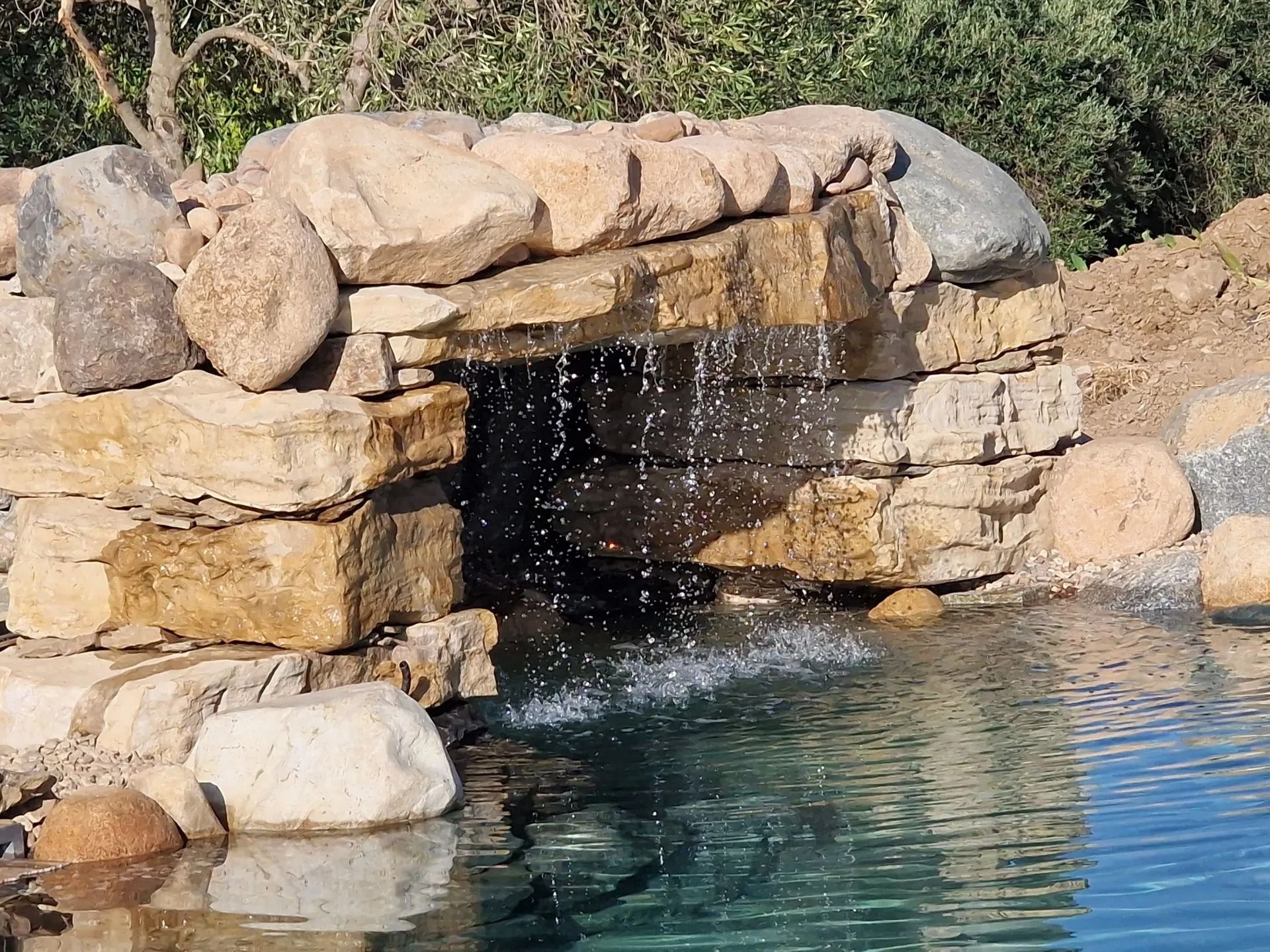 Una piccola cascata che si riversa in uno stagno limpido, di colore blu-verde, costituito da rocce marrone chiaro.