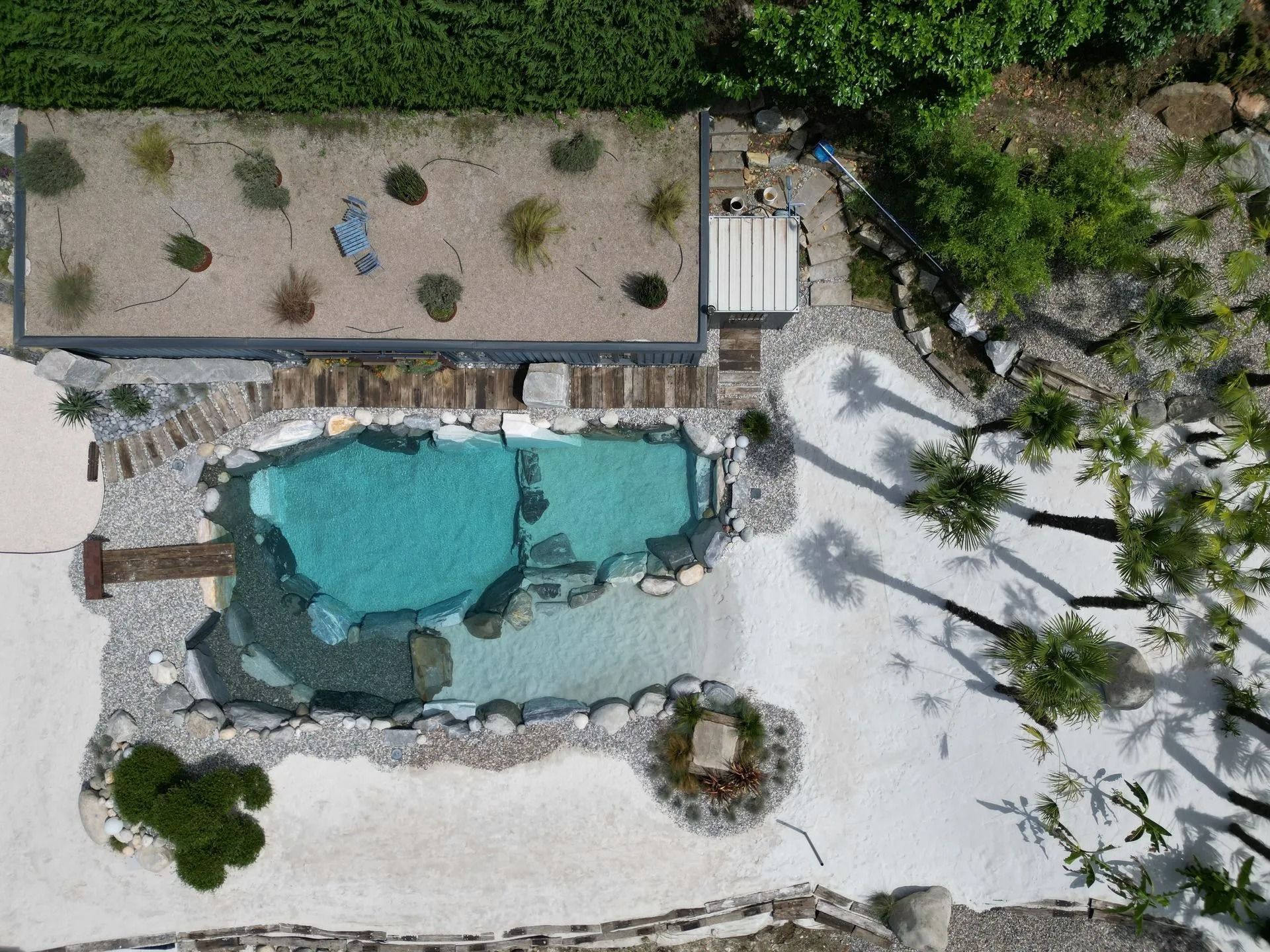Vista aerea di una piscina turchese circondata da rocce, un giardino pensile e ghiaia bianca.