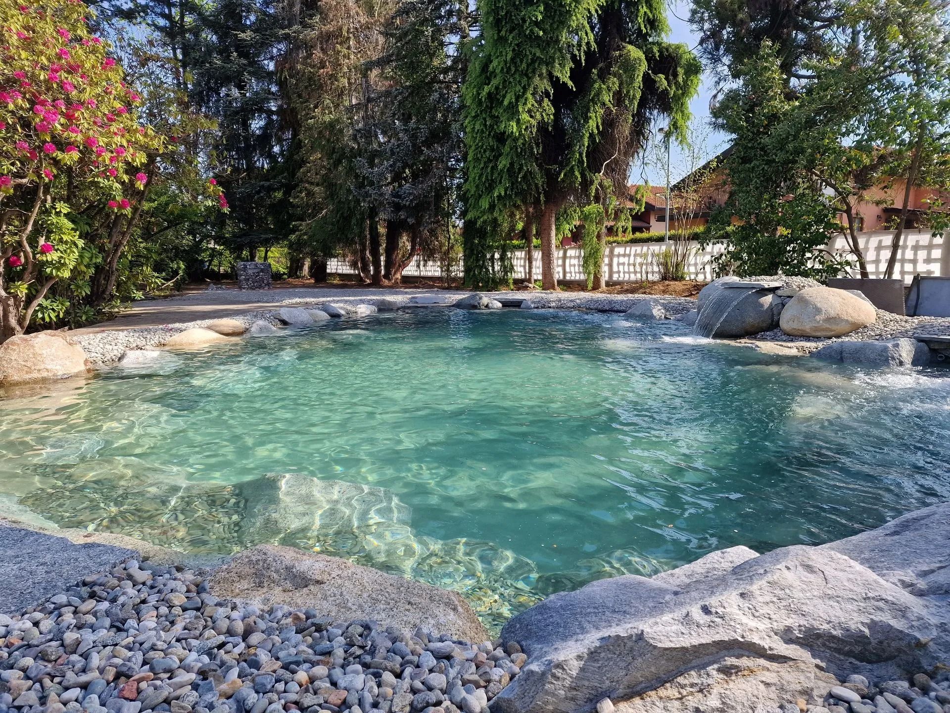 Tranquilla piscina turchese circondata da rocce, alberi e vegetazione lussureggiante; cascate che si riversano nell'acqua.