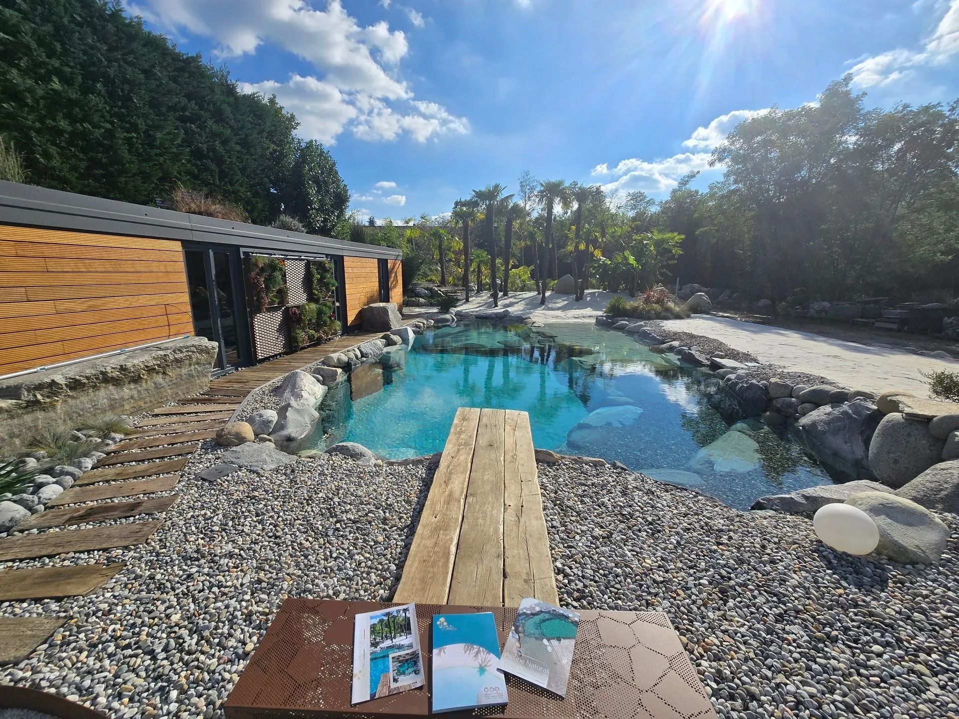 Un molo di legno sopra una piscina turchese con rocce e alberi sotto un cielo soleggiato.