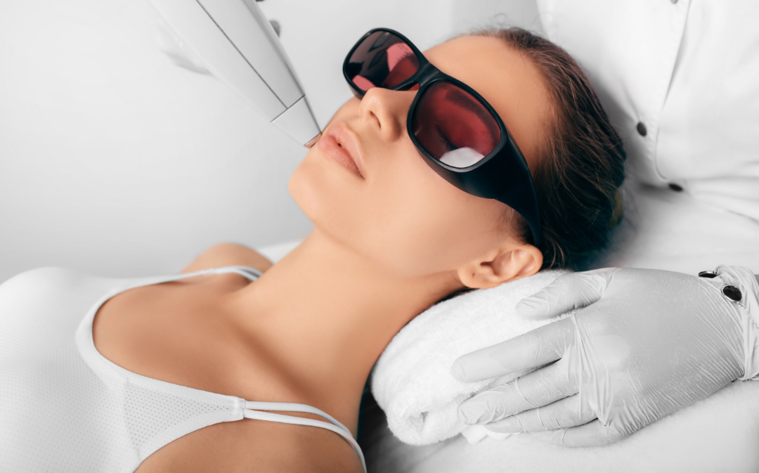 Mulher usando óculos de proteção durante um tratamento a laser em um spa, deitada em uma cama branca.
