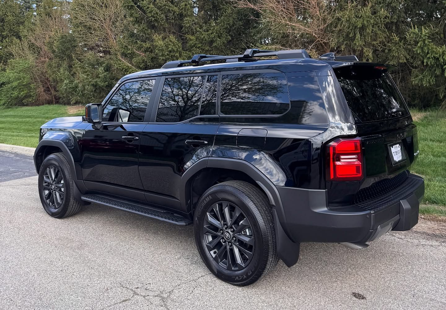 Black Land Rover Defender parked on asphalt with trees and cloudy sky.