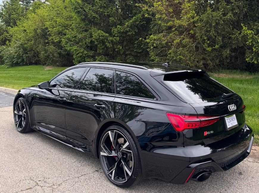 Black Audi RS6 Avant parked on asphalt next to greenery.