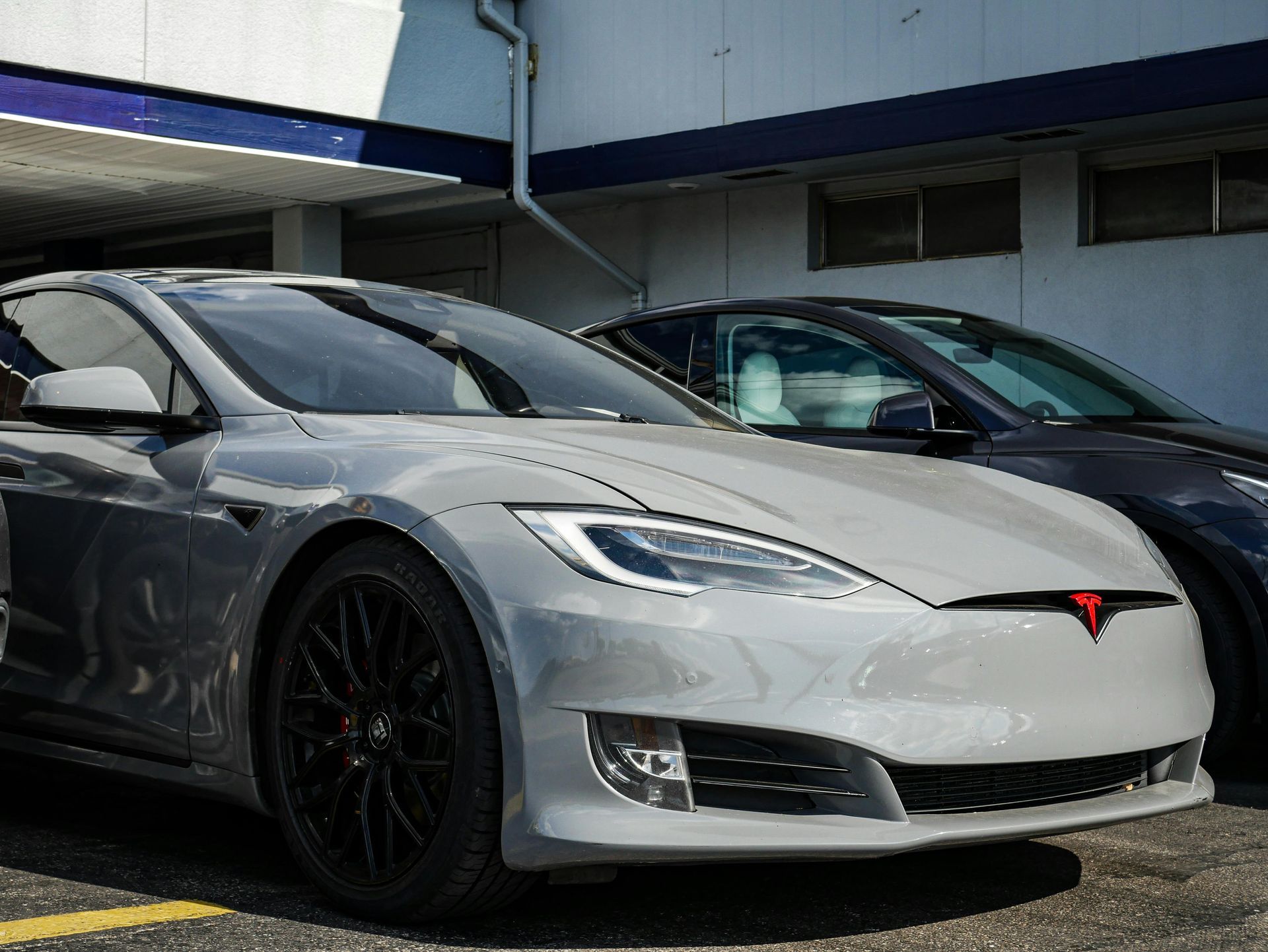 A grey Tesla Model S parked outdoors with black wheels and a custom red front emblem.