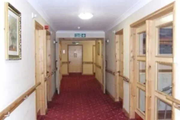 Hallway with red carpet, light wood doors and handrails, likely in a care facility.