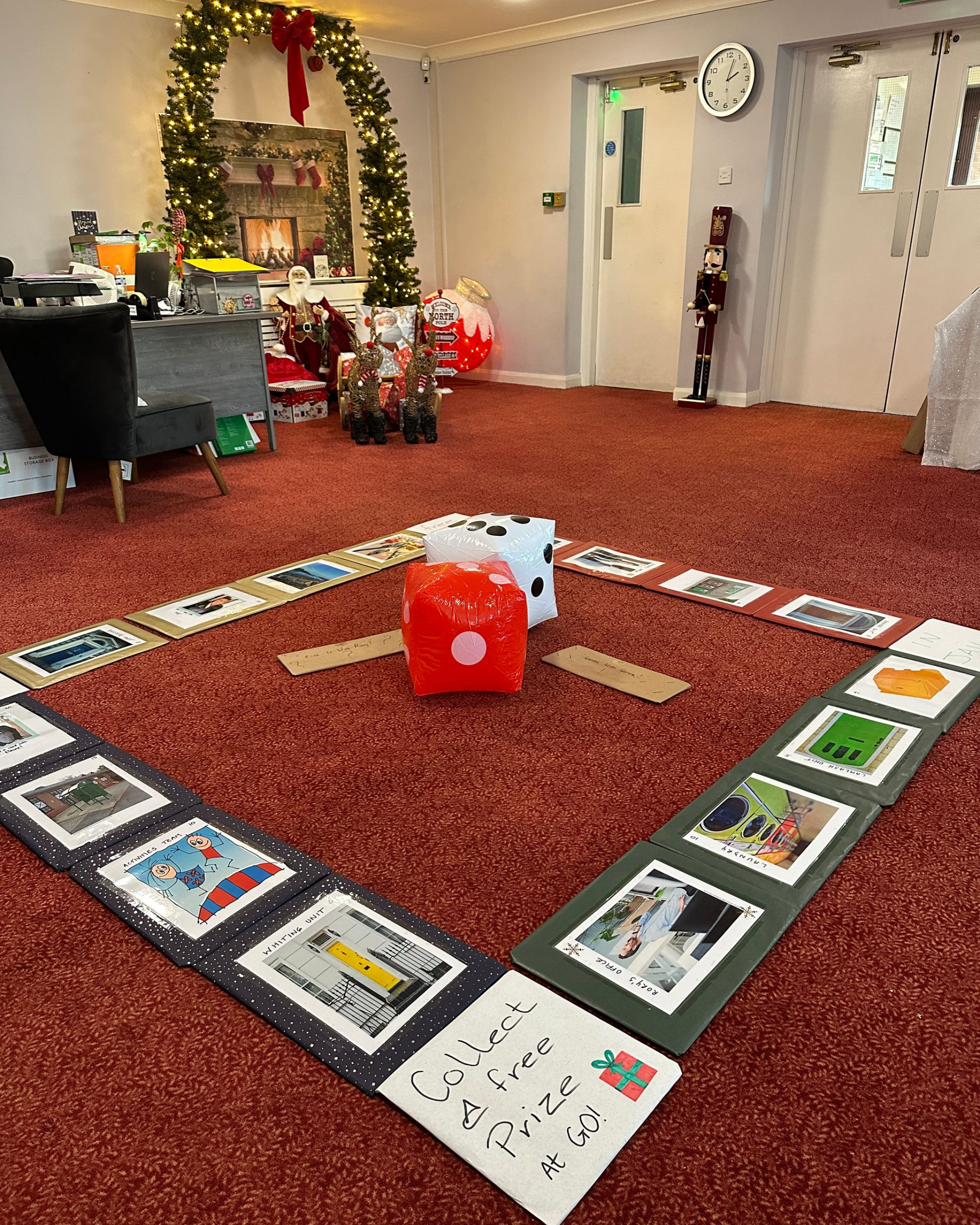Room decorated for the holidays, with a game board on the red carpet floor, and two large dice in the centre.