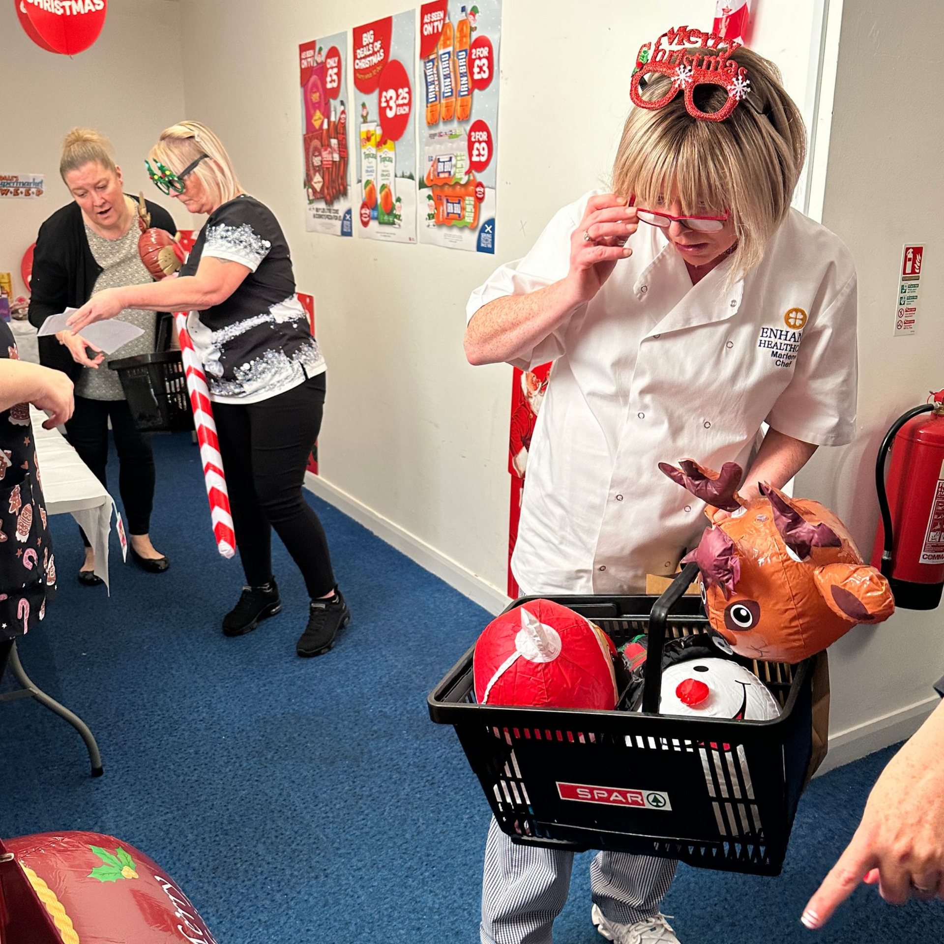 People playing a Christmas game, one holding a basket of festive masks in a decorated room with red and white decorations.
