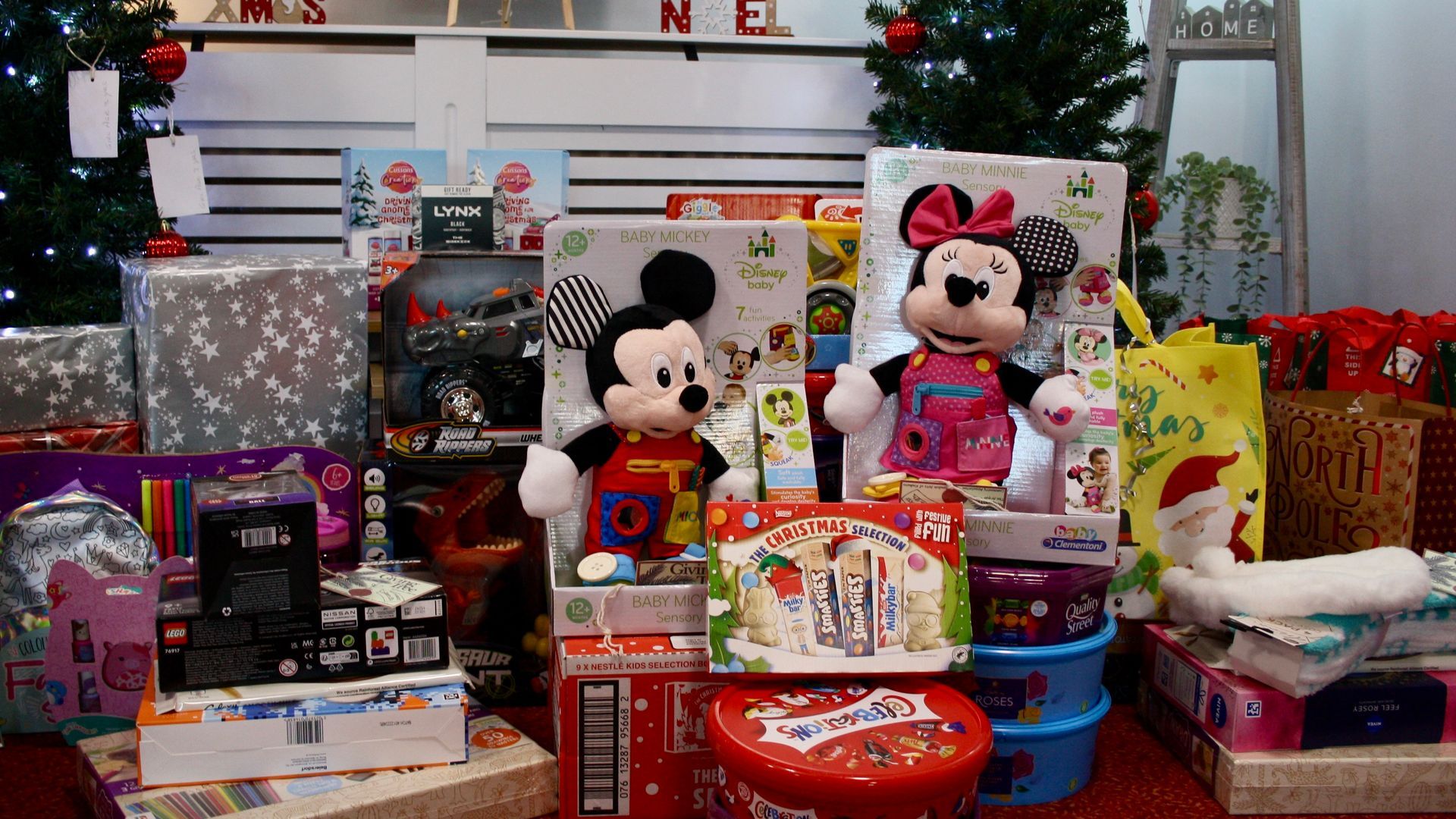 A pile of christmas presents including mickey mouse and minnie mouse are sitting under a christmas tree.