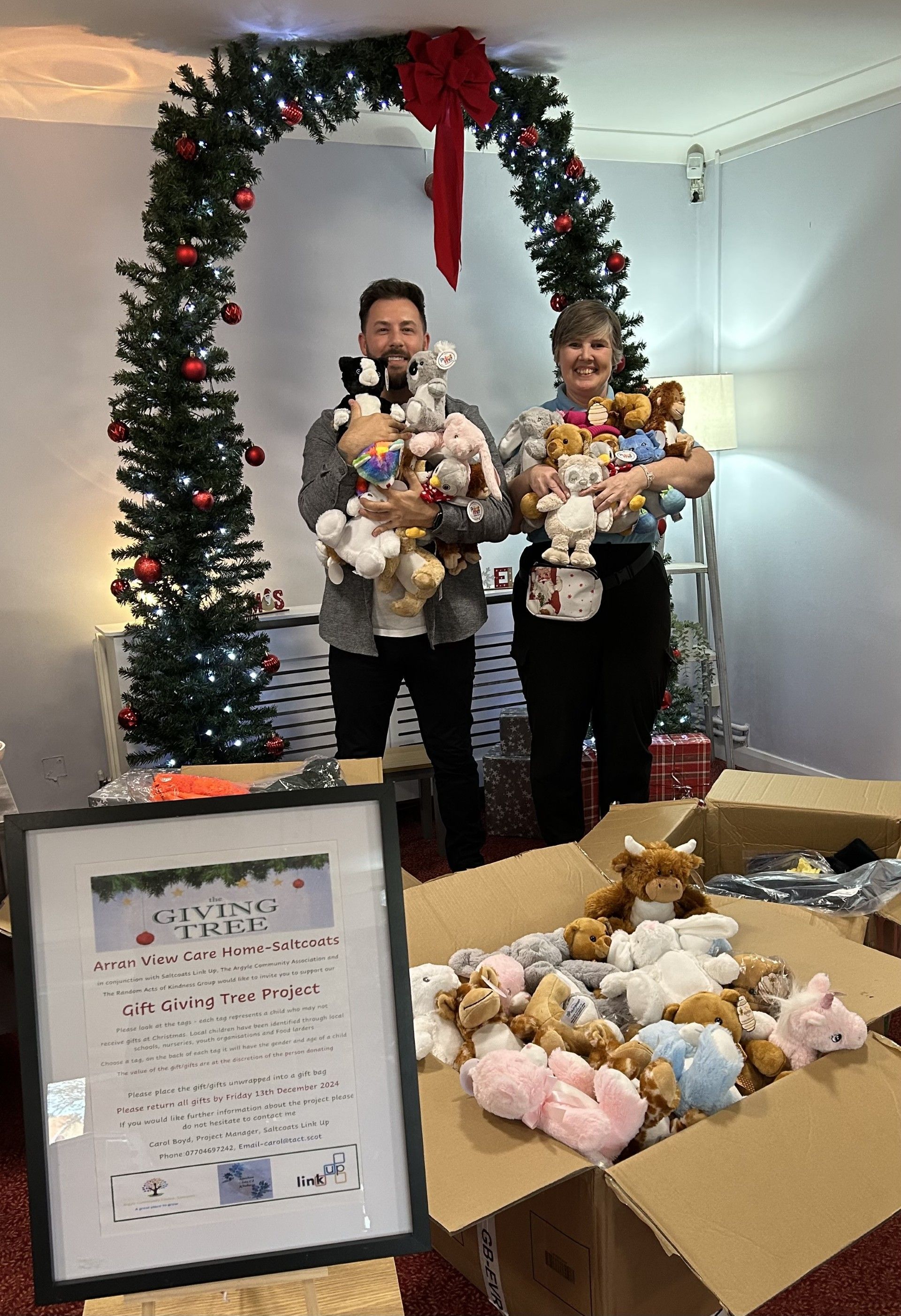 A man and a woman are holding stuffed animals in front of a christmas tree.