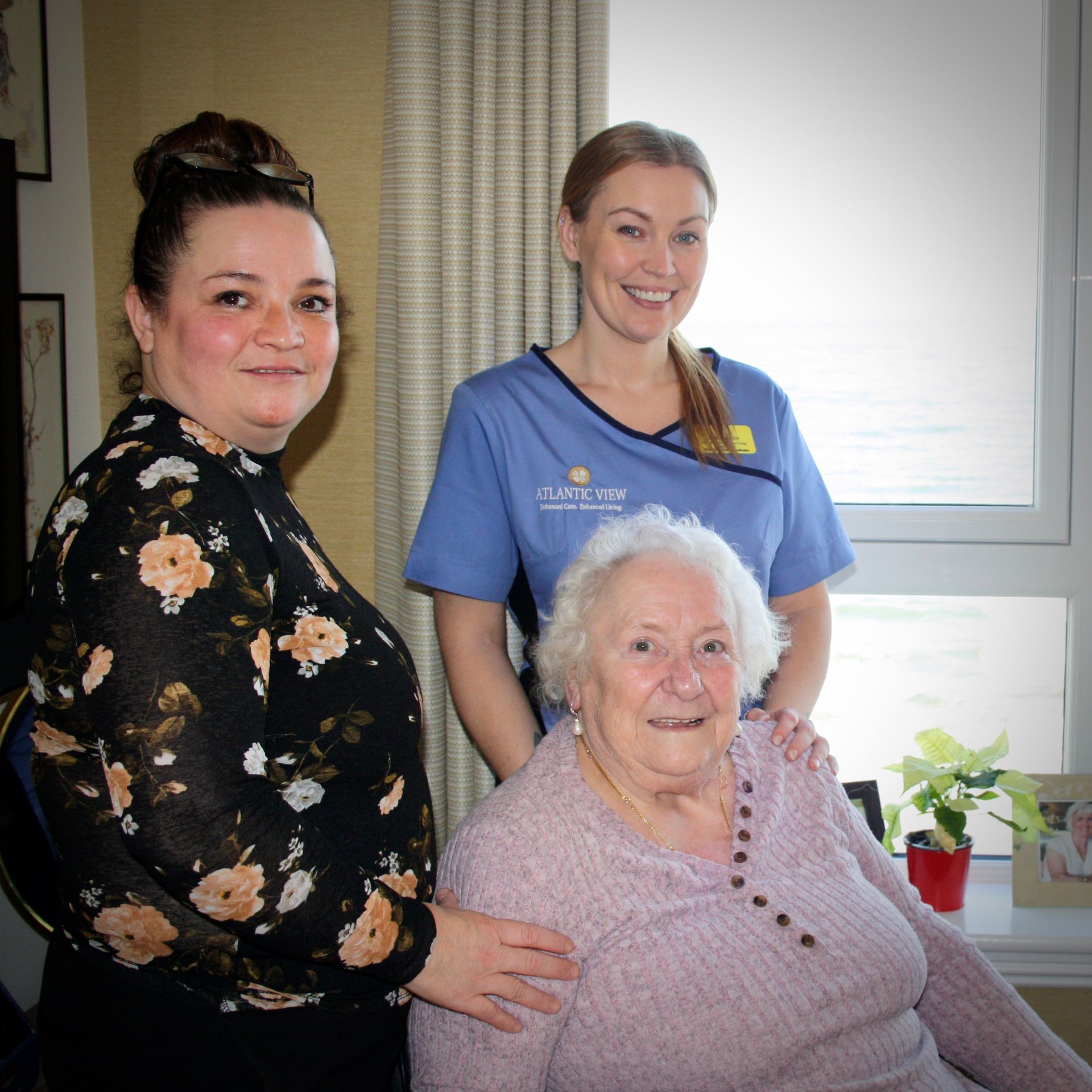 Two women and an elderly woman are posing for a picture in front of a window