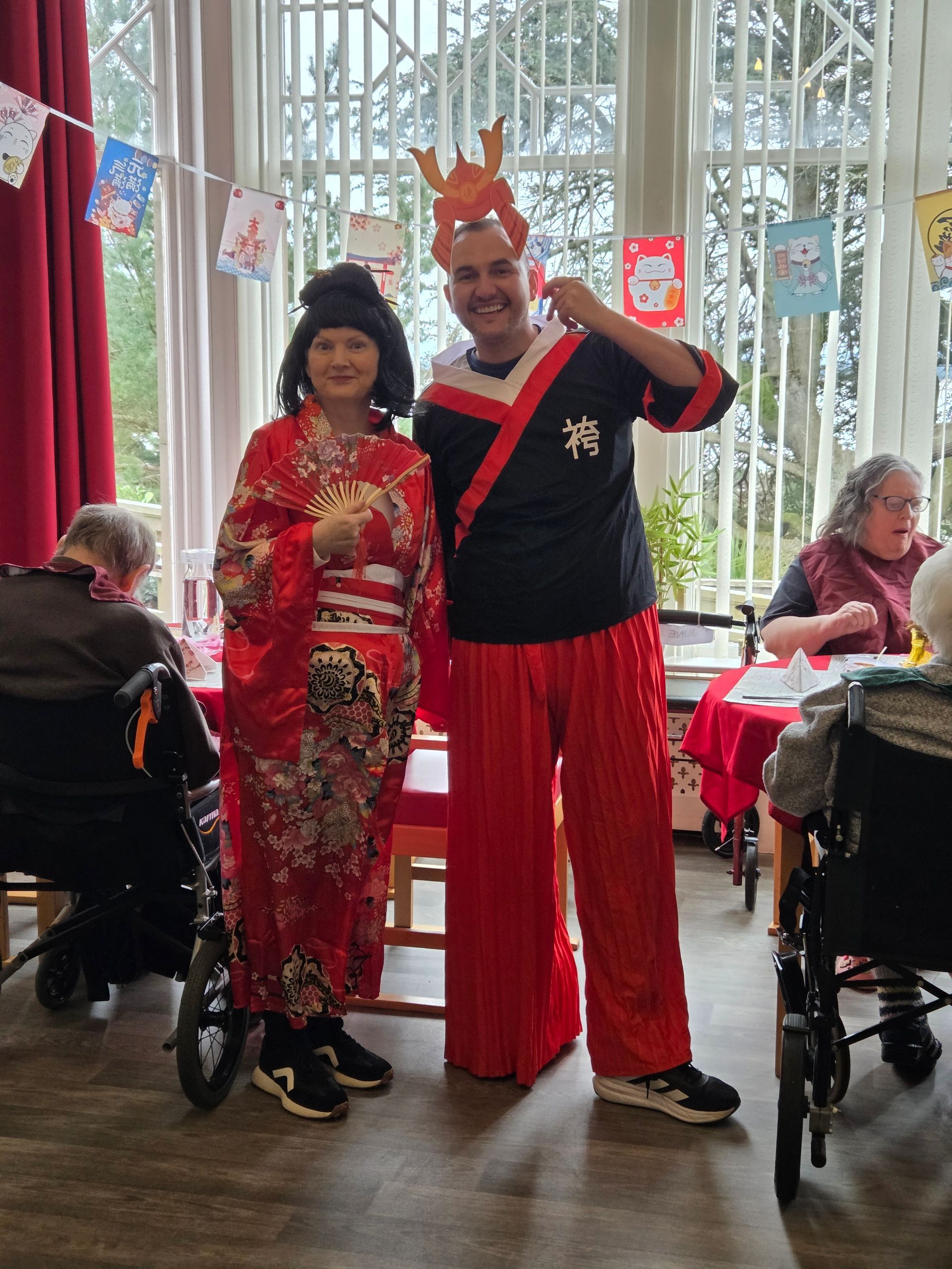 A man and a woman are posing for a picture in a room with people in wheelchairs.