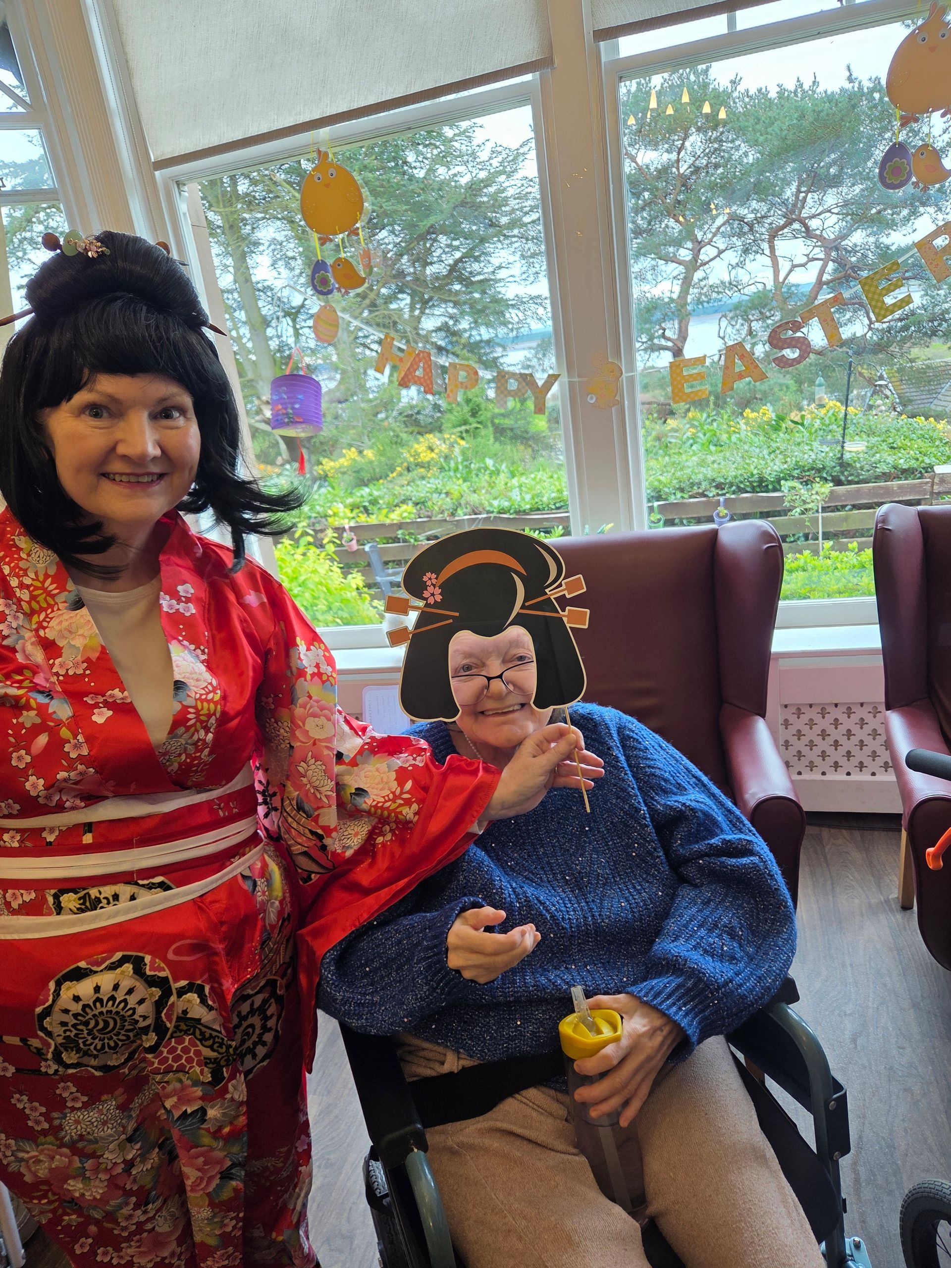 A woman in a kimono is standing next to a woman in a wheelchair.
