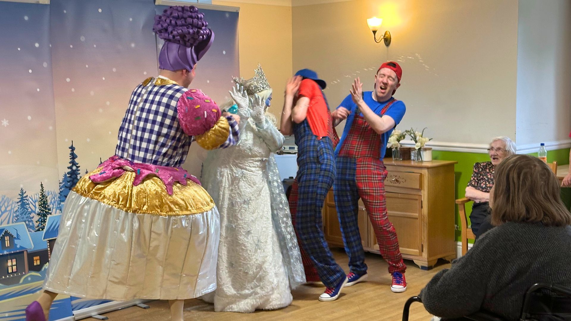 Performers in colourful costumes act out a scene in front of a painted winter backdrop.