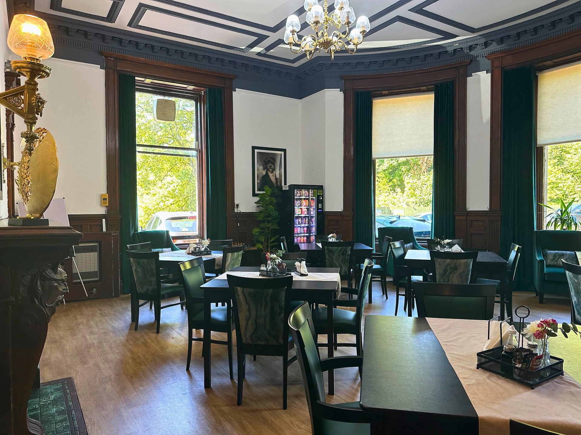 Restaurant interior with dark wood trim, green curtains, tables, chairs, and a chandelier.