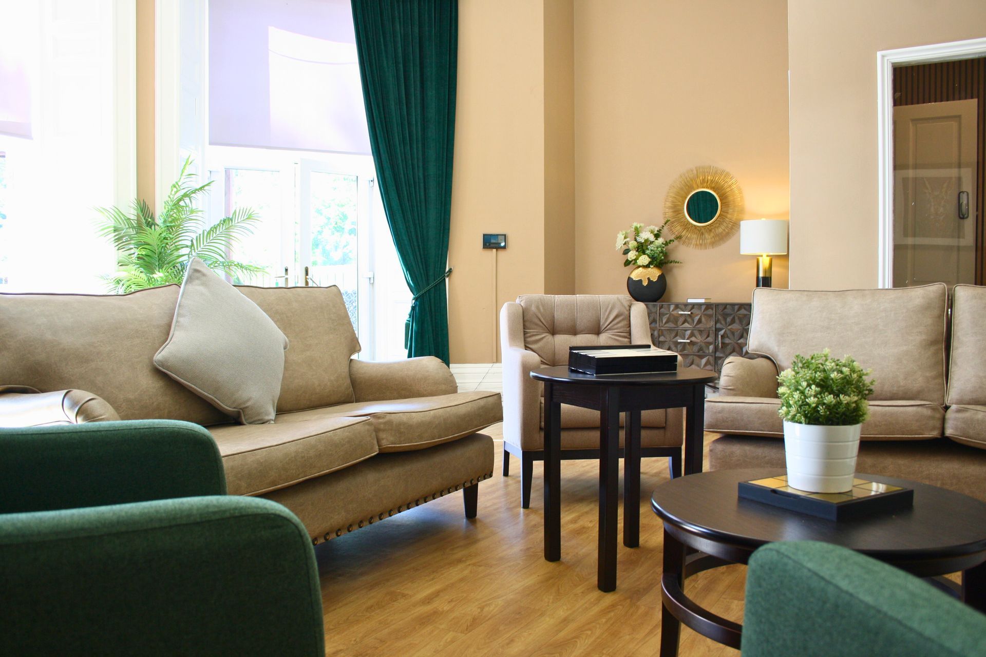 Living room with tan couches, green chairs, wood tables, teal curtains, and a doorway.
