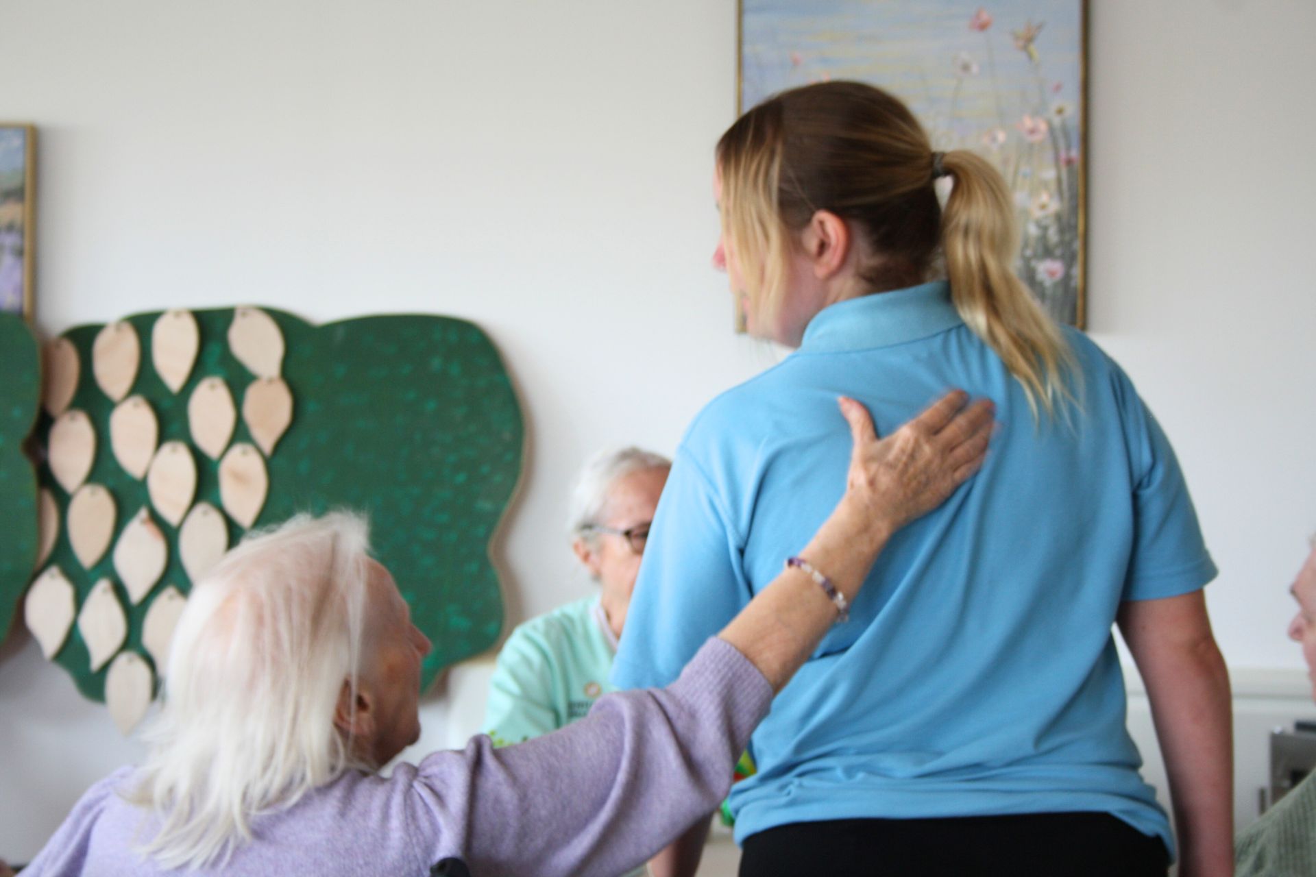 A woman in a blue shirt is standing next to an older woman in a wheelchair.