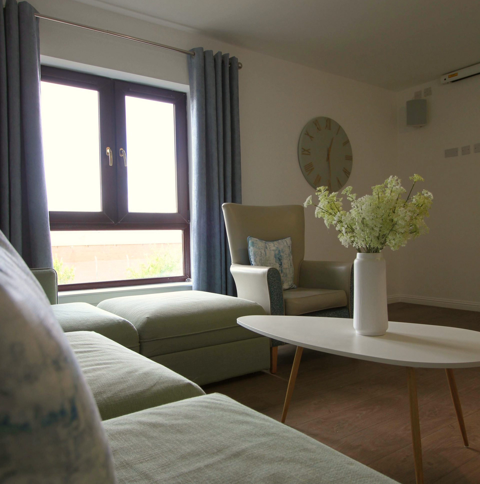 A living room with a clock on the wall and a vase of flowers on the table