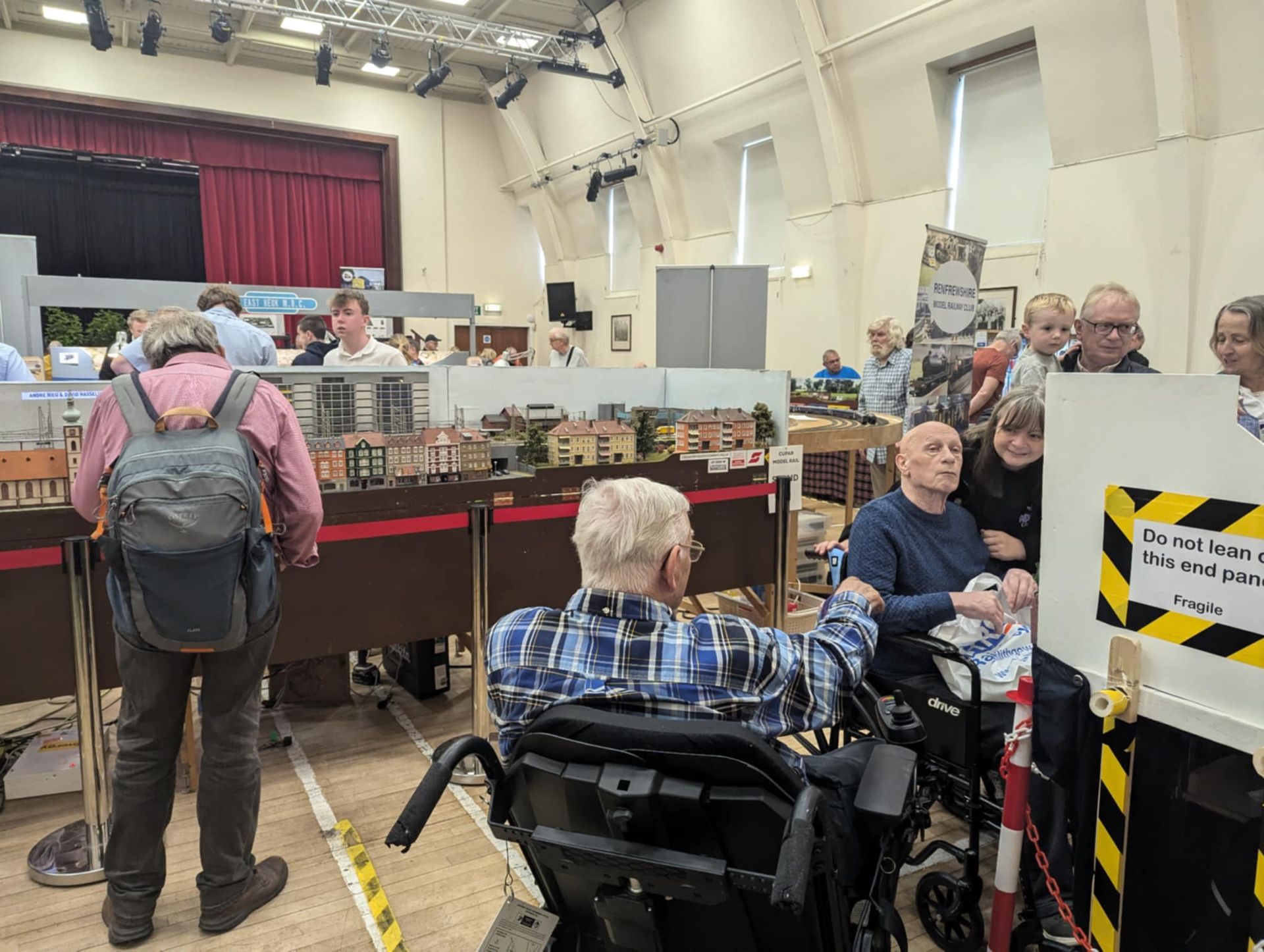 People viewing a model railway display at an event. One man uses a wheelchair.