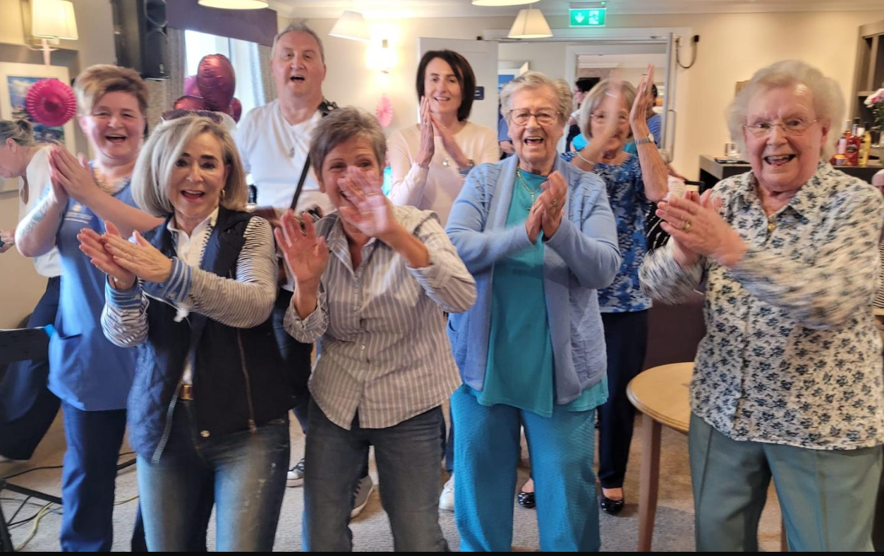 A group of people are standing in a room clapping their hands.