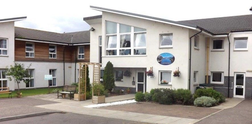 Exterior view of a white building with several windows and a dark roof; a sign is visible.