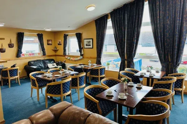 A restaurant dining area with tables and chairs near large windows with dark blue curtains; a blue carpet.