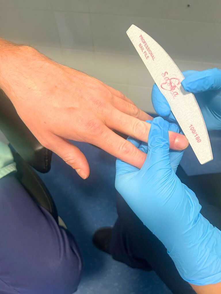 A person wearing blue gloves is filing another person 's nails