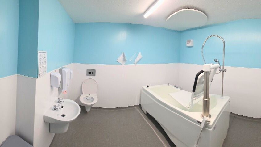 A medical treatment room with blue and white walls, a bathtub, toilet, and sink.