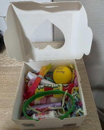 White gift box with a heart-shaped cutout, filled with sweets and small toys.