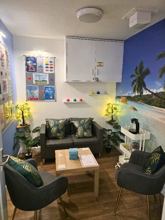 Cozy waiting room with a sofa, chairs, small table, and tropical mural.