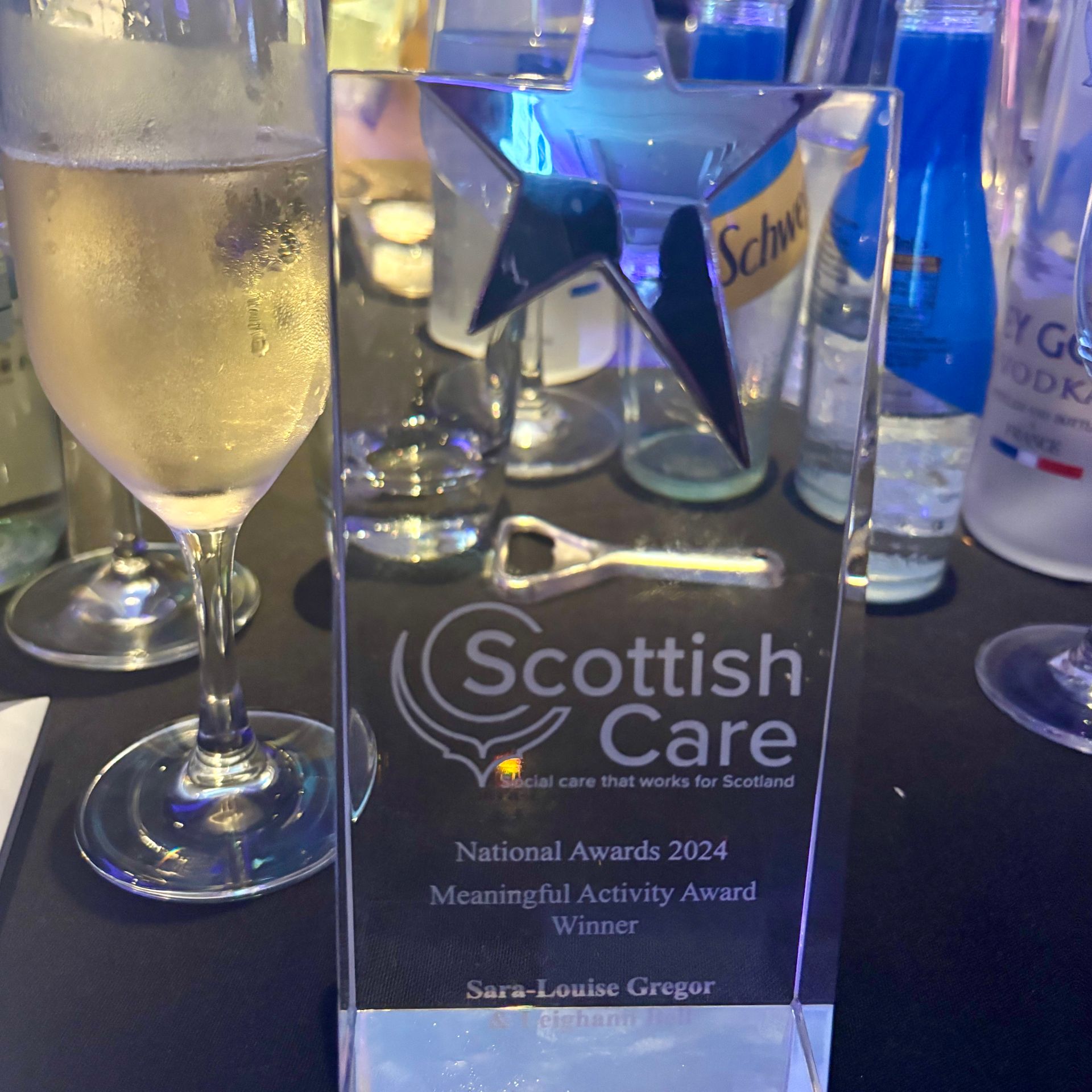 A scottish care award is sitting on a table next to wine glasses.