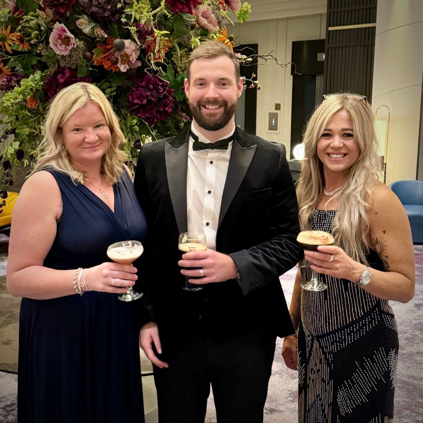 A man and two women are standing next to each other holding champagne glasses.