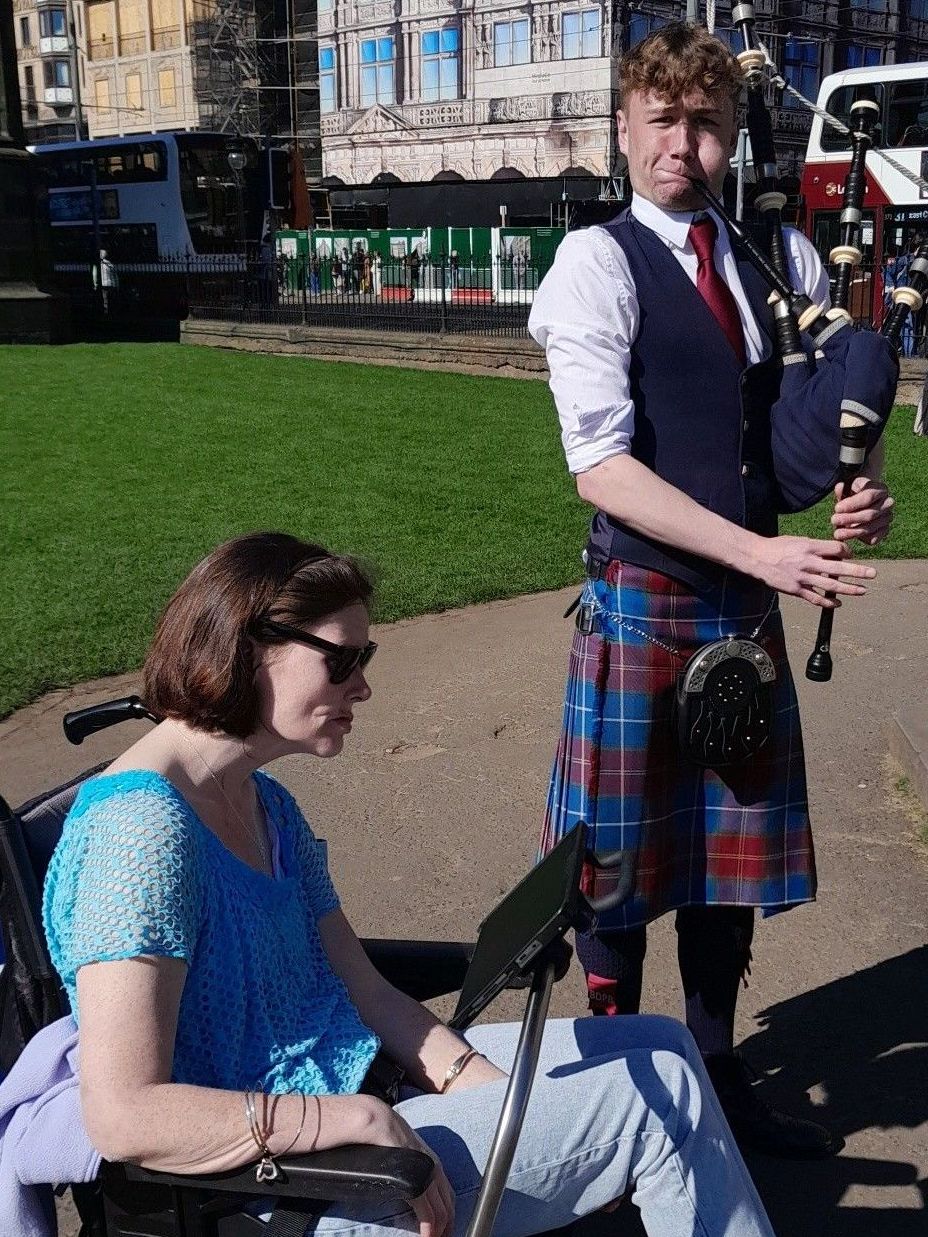 A man in a kilt is playing bagpipes next to a woman in a wheelchair