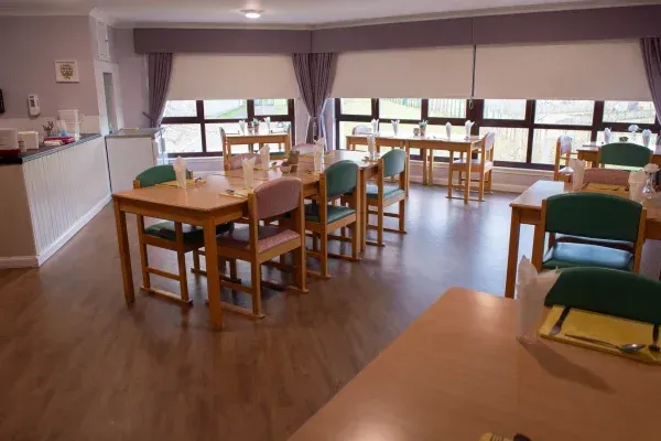 Dining room with several tables, chairs, and windows. Some tables have place settings. The room has neutral colors.