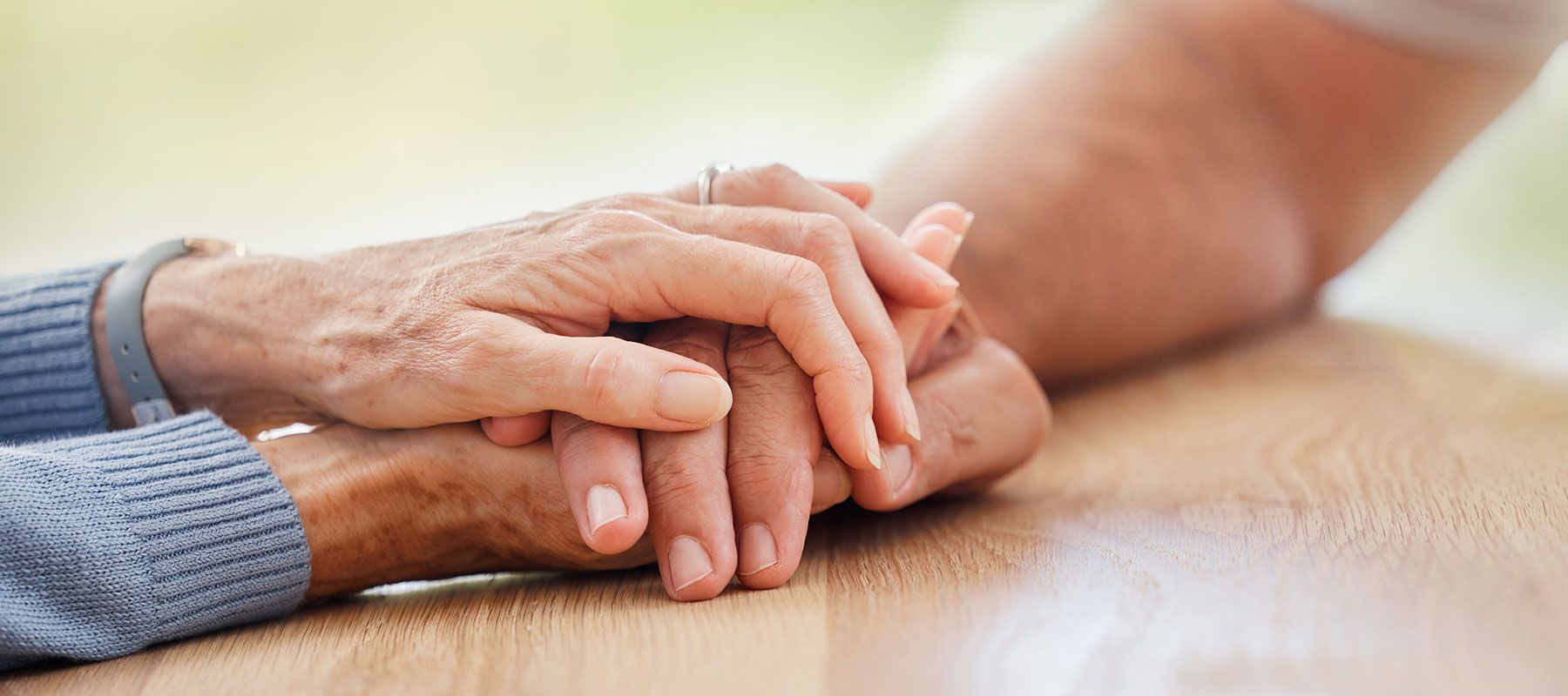 A woman is holding an older woman 's hand on a wooden table.