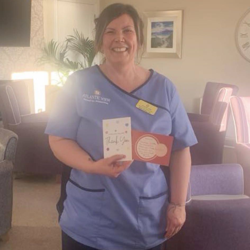 A woman in a blue scrub top is holding a thank you card.