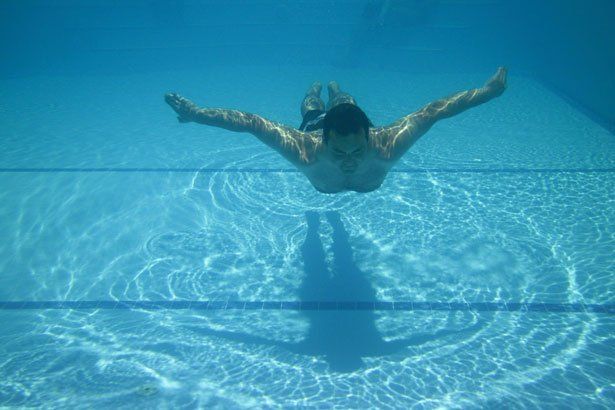 A man is swimming underwater in a swimming pool.