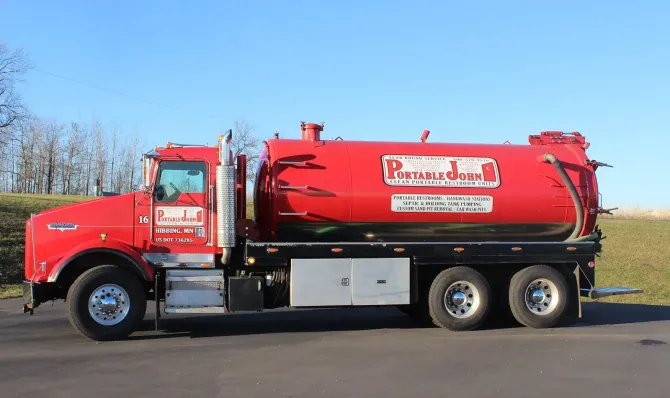 A bright red vacuum tanker truck parked on an asphalt road against a clear blue sky. A bright red vacuum tanker truck parked on an asphalt road against a clear blue sky.