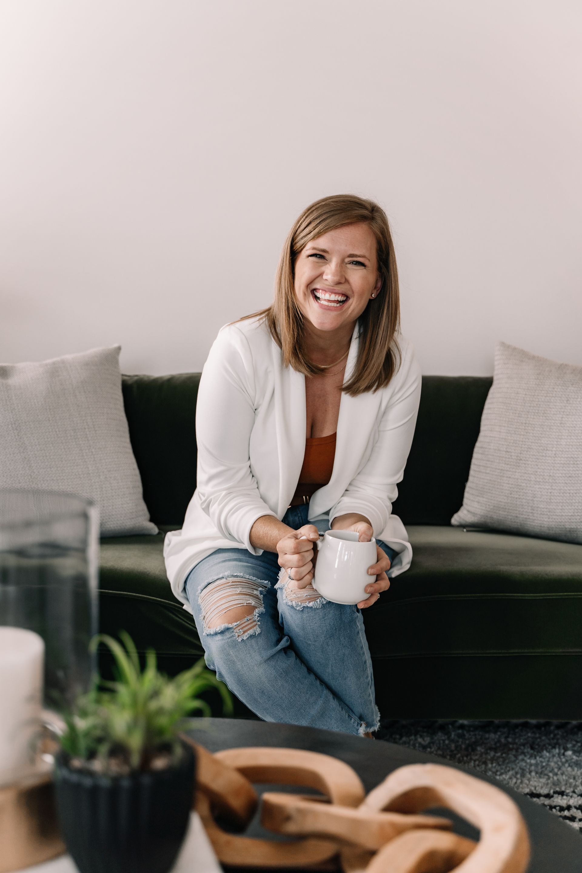 A woman is sitting on a couch holding a cup of coffee.