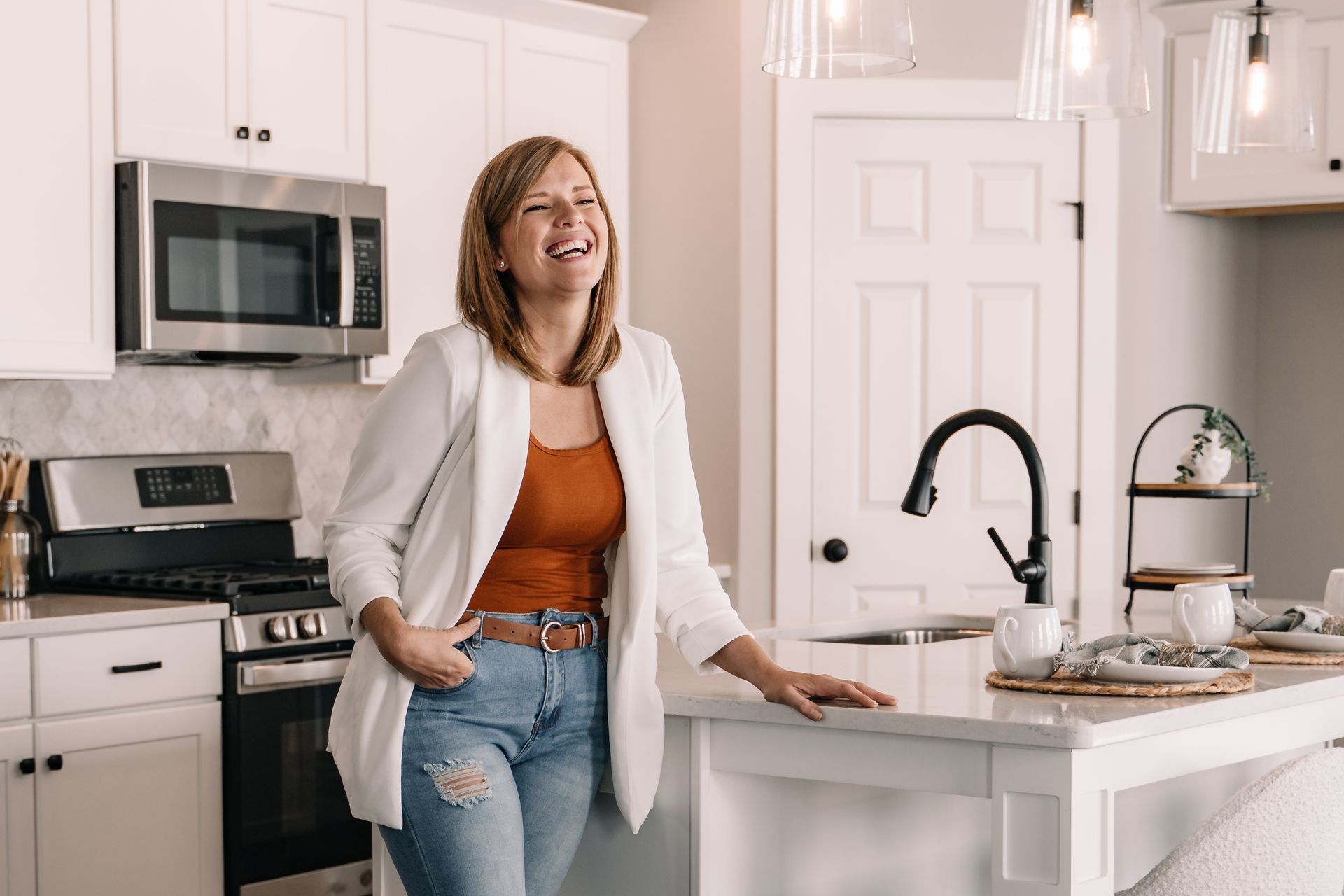 A woman is standing in a kitchen with her hands in her pockets.