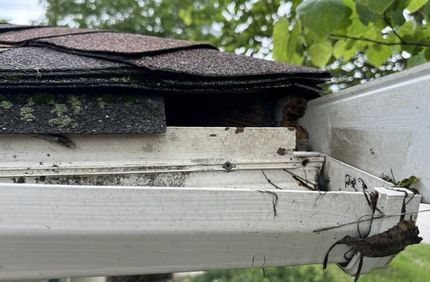 A close up of a gutter with a roof in the background.