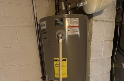 A gray water heater is sitting on top of a white brick wall.