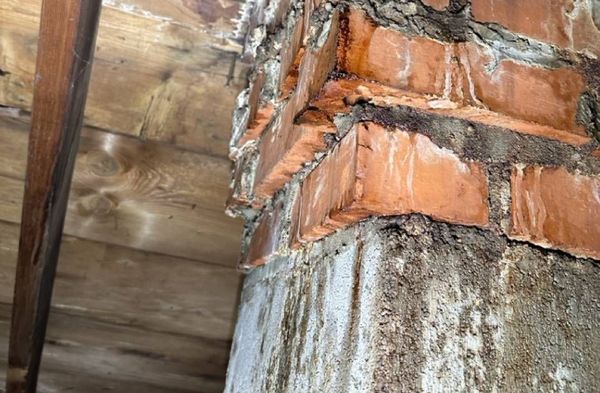 A close up of a brick chimney with a wooden ceiling in the background.