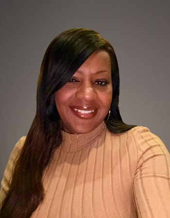 Woman with long dark hair, smiling, wearing a tan turtleneck. Grey background.